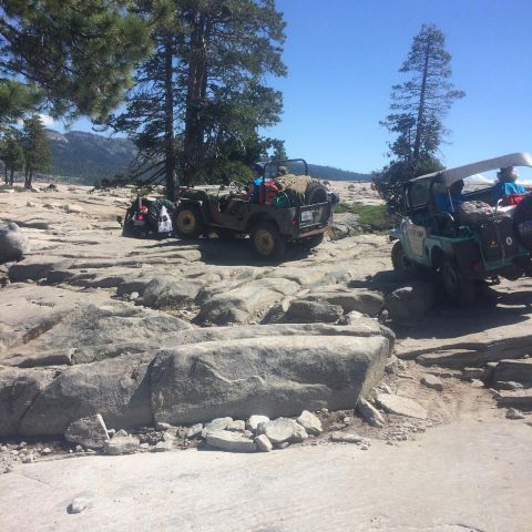 1946 Jeep CJ5 - Two vintage Jeeps navigate a rocky trail in a mountainous area, loaded with gear for an off-road adventure.
