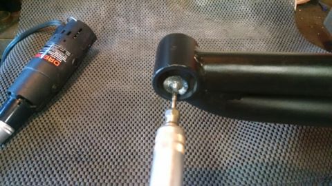 1992 Ford Bronco - A Dremel rotary tool is used to clean the interior of a black metal suspension component, likely an extended radius arm.