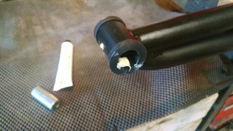 1992 Ford Bronco - A close-up view of a black metal suspension component being prepared with grease, alongside a tube of lubricant.