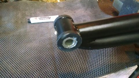1992 Ford Bronco - A close-up view of a black suspension arm with a rubber bushing, alongside a tube of lubricant.