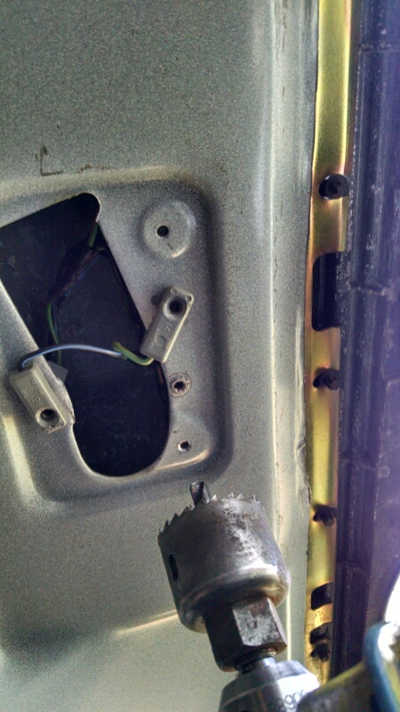 1992 Ford Bronco - Close-up of a vehicle's interior door panel showing wiring and a hole saw bit, likely for installing a light.