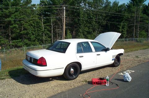2001 Ford Crown Victoria - White 2001 Ford Crown Victoria with hood open, parked on a dirt shoulder next to a road.