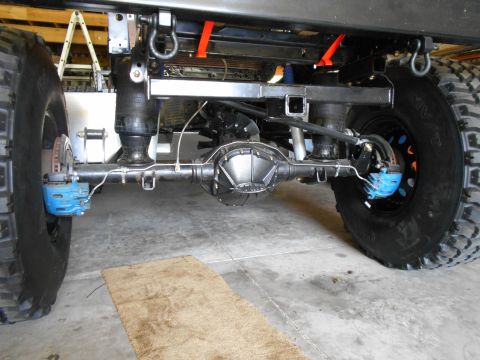 1992 Ford Bronco - Close-up view of the rear axle, suspension, and large tires of a vehicle, with visible blue brake calipers.