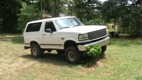 1996 Ford Bronco - This white Ford Bronco is parked in a grassy area with trees surrounding it.