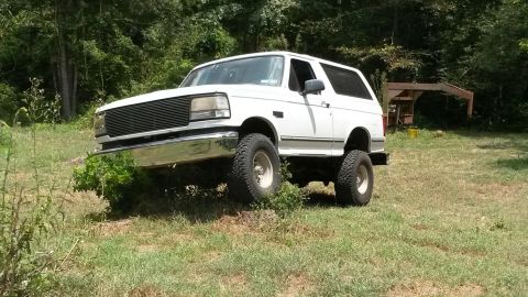 1996 Ford Bronco - A white Ford Bronco is shown from a 3/4 front angle, parked on a grassy hill with trees in the background.