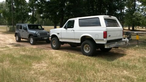 1996 Ford Bronco - A white 1996 Ford Bronco is parked next to a grey Jeep Wrangler in a grassy, outdoor area.