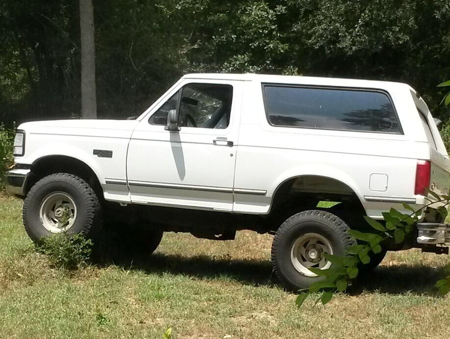 White 1996 Ford Bronco parked on grassy terrain, side view
