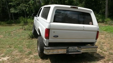 1996 Ford Bronco - Rear view of a white 1996 Ford Bronco parked in a grassy area with trees in the background.