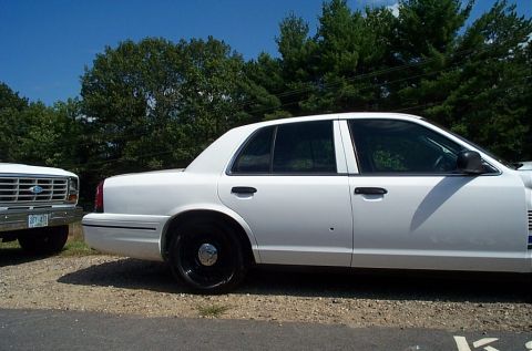 2001 Ford Crown Victoria - A white sedan with black wheels is parked next to a white pickup truck on a sunny day.
