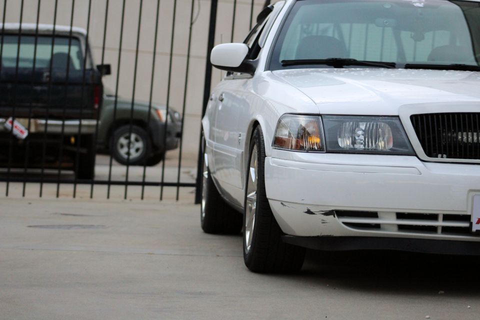 White sedan with scraped front bumper, seen from a low angle