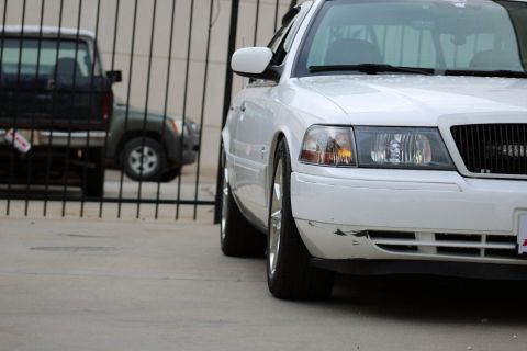 2000 Mercury Grand Marquis - A white sedan is parked in front of a fence, with a black truck visible behind it.