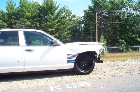 2001 Ford Crown Victoria - A damaged white 2001 Ford Crown Victoria is parked outdoors with trees and a fence in the background.