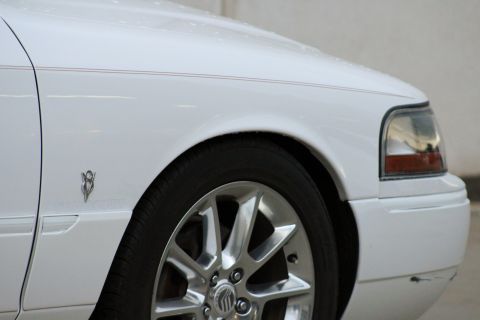 2000 Mercury Grand Marquis - Close-up of the front fender and chrome wheel on a white 2000 Mercury Grand Marquis, a V8 badge.