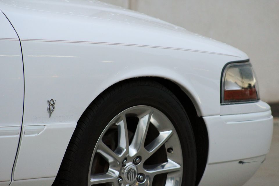 White 2000 Mercury Grand Marquis fender with chrome wheel and V8 badge