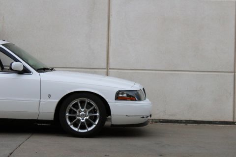 2000 Mercury Grand Marquis - Front quarter view of a white 2000 Mercury Grand Marquis with custom chrome wheels parked against a concrete wall.