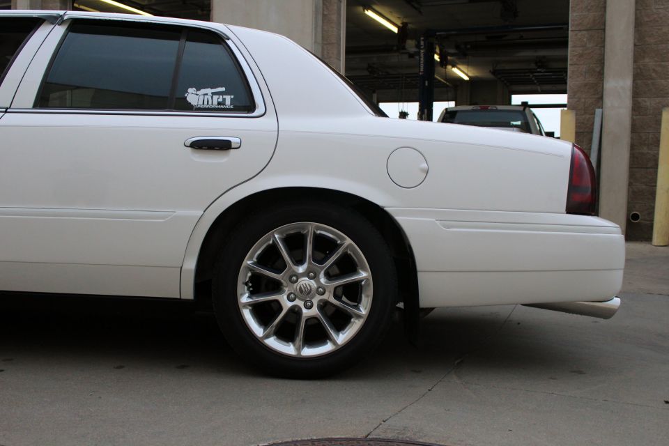 White sedan rear quarter panel with chrome wheels and a sticker on the rear window