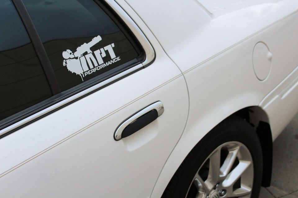 White sedan's rear passenger door and window, showing a chrome door handle and a white performance sticker