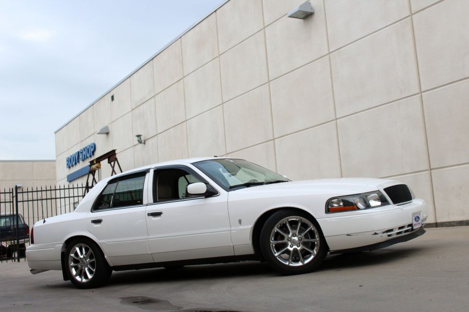 White sedan parked in front of a building with "BODY SHOP" sign, 3/4 front view