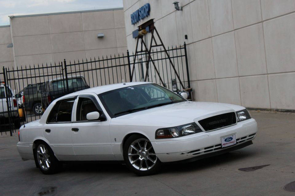 White 2000 Mercury Grand Marquis parked in front of a building, with another vehicle visible behind a fence