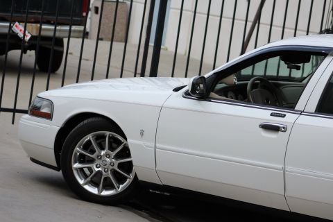 2000 Mercury Grand Marquis - A white sedan is parked behind a black fence, with another vehicle partially visible in the background.