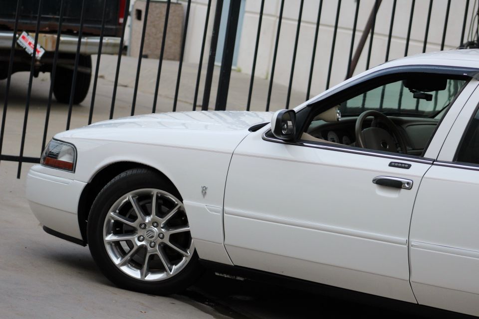 White sedan with chrome wheels, front fender, door, and interior visible