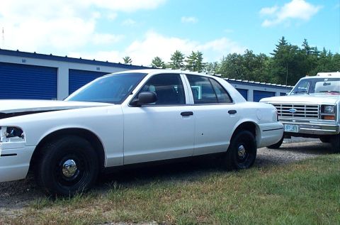 2001 Ford Crown Victoria - A white sedan and a white pickup truck are parked in front of blue storage unit doors on a sunny day.