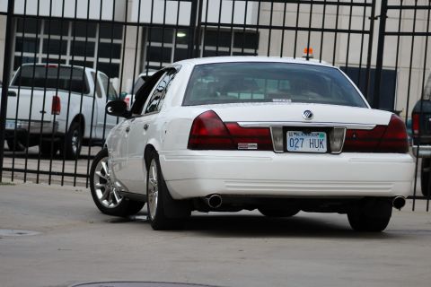 2000 Mercury Grand Marquis - Rear view of a white 2000 Mercury Grand Marquis, custom wheels and dual exhaust pipes, parked behind a fence.