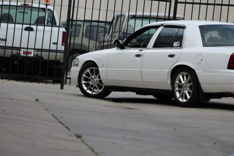 2000 Mercury Grand Marquis - A white sedan is parked behind a fence, with other vehicles partially visible.