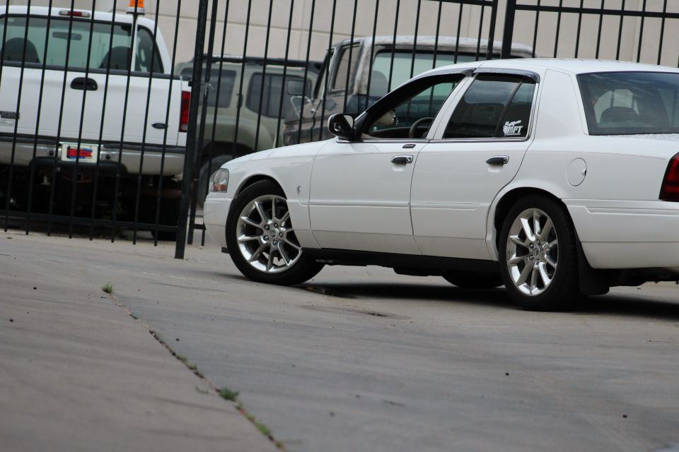 White sedan parked behind a fence with a white pickup truck and a dark SUV visible