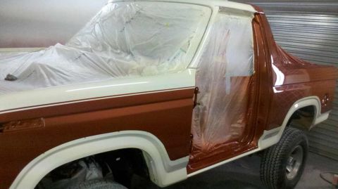1982 Ford Bronco - A two-tone brown and white Ford Bronco is shown from the front three-quarter view, with plastic sheeting covering parts of the vehicle duri…