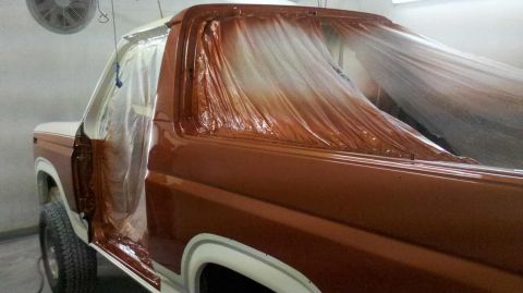 1982 Ford Bronco - Bronco undergoing paint work in a spray booth, doors ajar and covered for protection.