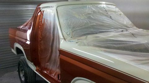 1982 Ford Bronco - A two-tone brown and white Ford Bronco is covered in plastic sheeting, indicating it is in a paint booth for bodywork.