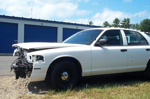 2001 Ford Crown Victoria - A white 2001 Ford Crown Victoria shows extensive damage to its front end, parked outdoors.