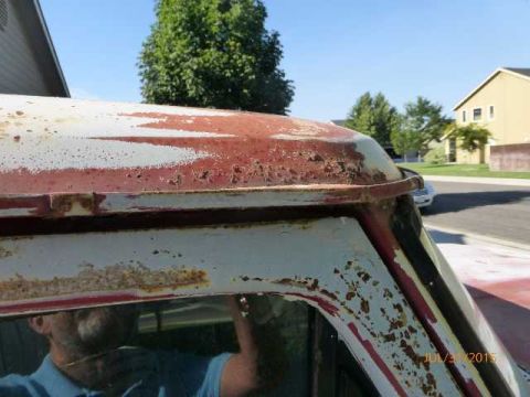 1970 Ford F-250 - This photo shows significant rust damage on the cab corner of a truck, with a reflection of a person in the window.