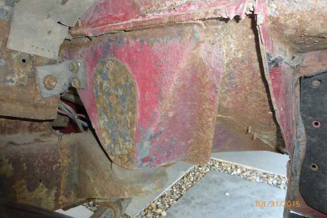 Heavily rusted red vehicle frame components with visible wiring and bolts. The view is a close-up of the undercarriage