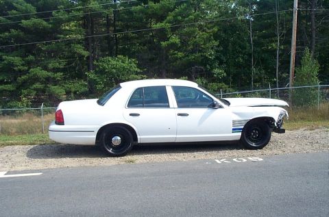 2001 Ford Crown Victoria - A white sedan is parked on the side of the road with damage to its front end.