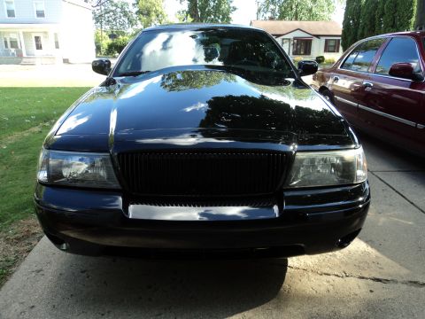 2004 Mercury Grand Marquis - The front view of a black Mercury Grand Marquis is shown, parked on a concrete driveway with a lawn and houses in the background. A maroon…