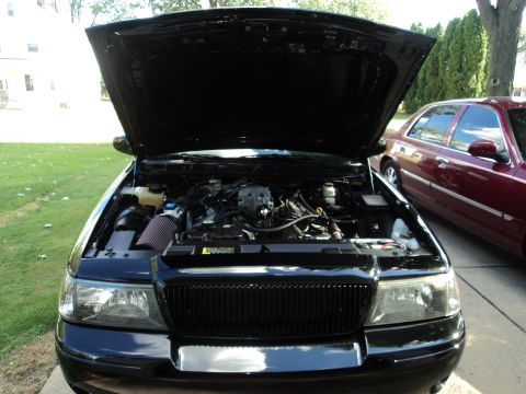 2004 Mercury Grand Marquis - Black Mercury Grand Marquis with open hood revealing the V8 engine bay and aftermarket cone intake outdoors.