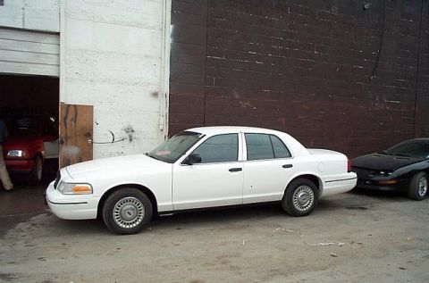 2001 Ford Crown Victoria - Side view of a white 2001 Ford Crown Victoria parked outside a building.
