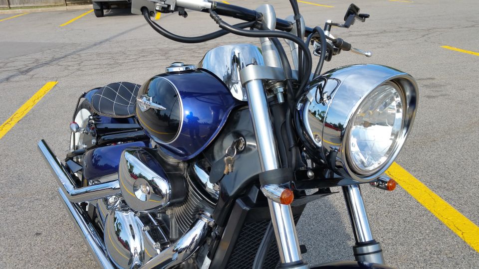 Close-up of dark blue cruiser motorcycle tank, chrome headlight and forks, keys in ignition, in a parking lot
