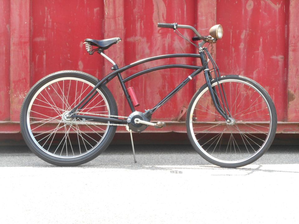 Black custom cruiser bicycle with vintage headlight against red wall