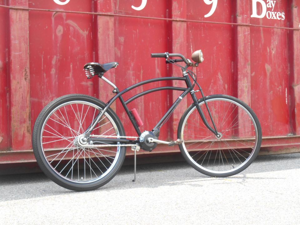 Black cruiser bicycle with vintage headlight parked in front of a red shipping container.