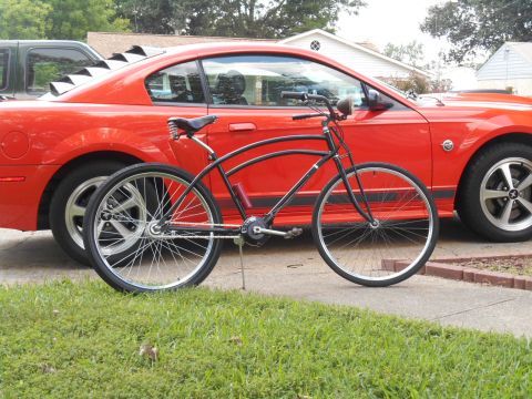 Black cruiser bicycle in front of a red Ford Mustang coupe.