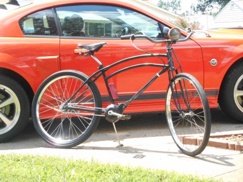 Black cruiser bicycle parked in front of an orange Ford Mustang.