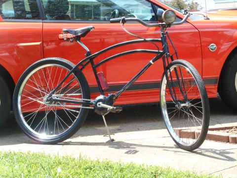 Black custom cruiser bicycle parked next to an orange Ford Mustang.