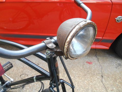 Close-up of bicycle handlebars and rusty headlight with red vehicle in background