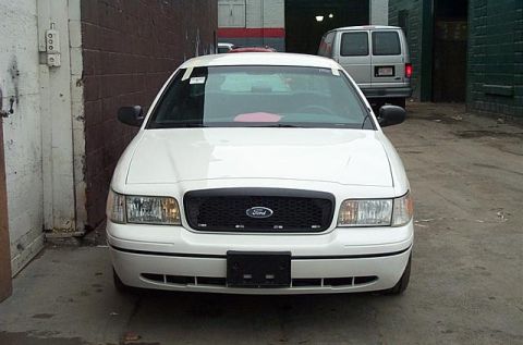 2001 Ford Crown Victoria - A white 2001 Ford Crown Victoria is parked in an alley, with a white van visible in the background.