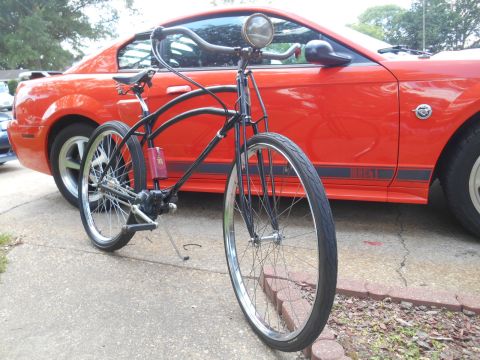 Black bicycle in front of an orange Ford Mustang with Mach 1 graphics.