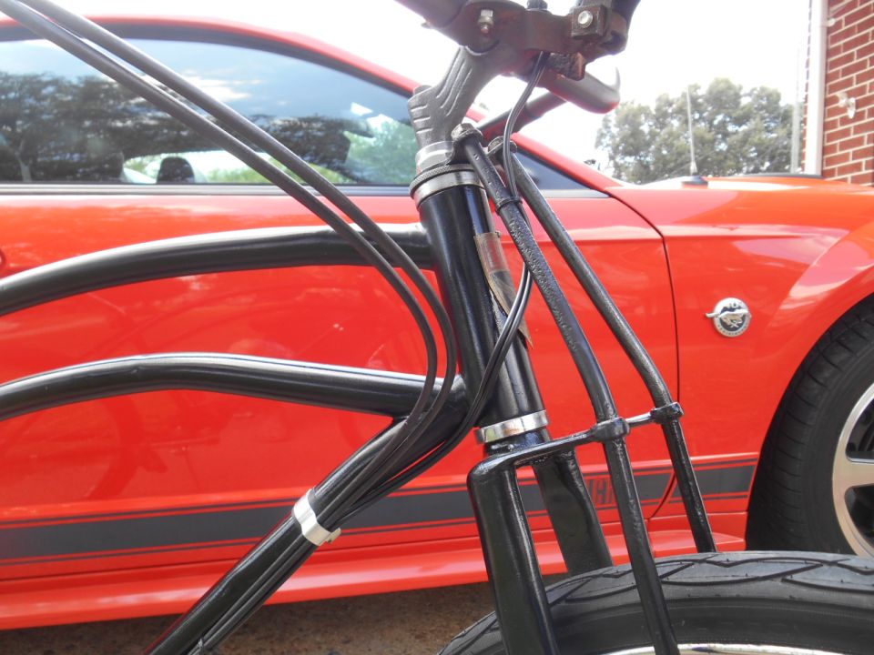 Black bicycle handlebars and cables in front of a red Ford Mustang.