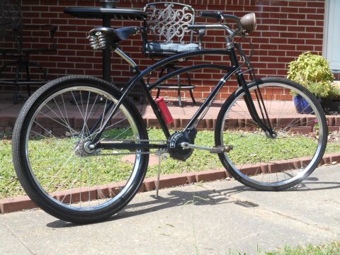 Black cruiser bicycle with red water bottle cage parked on sidewalk.